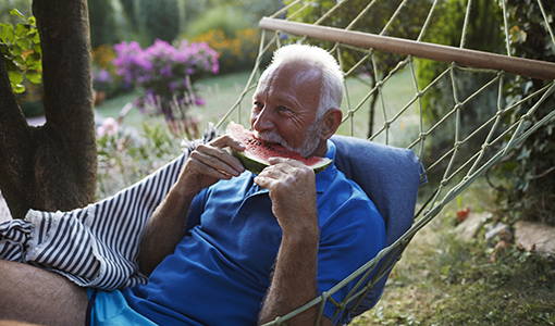 Senior man sitting in hammock and eating watermelon.