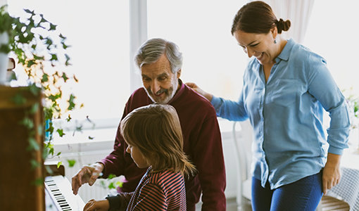 Happy mother and great grandfather looking at boy playing piano in house 