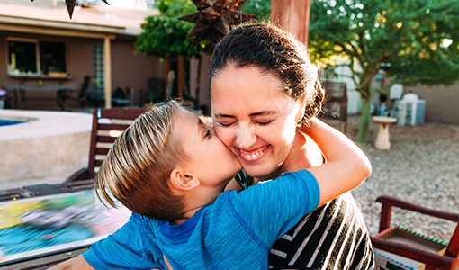 Young boy son hugging his smiling mother giving a kiss on the check.